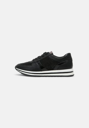 Sort sneaker med snørelukning, teksturerede og skinnende paneler samt en hvid sål med sorte striber, vist fra siden på en hvid baggrund.