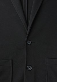 Blazer negro texturizado con cuello de solapa, dos bolsillos frontales y dos botones negros. La tela tiene un patrón tejido.