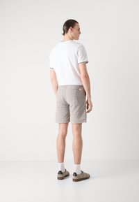 White polo shirt with black trim, paired with light gray linen shorts, visible back pockets, and brown shoes with black accents.