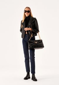 Black quilted handbag with a gold logo accent, paired with a black leather jacket, fitted black turtleneck, and dark jeans.
