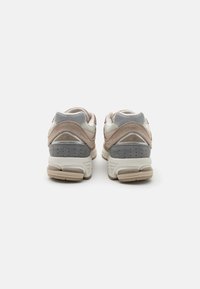 Baskets beiges et grises en daim et mesh, avec une semelle rembourrée, une forme arrondie et des accents de couture détaillés.