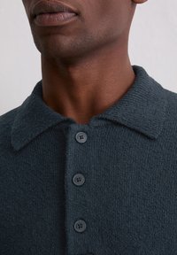 Granatowy teksturowany polo z kołnierzykiem, posiadający cztery dopasowane guziki oraz miękką, dzianinową tkaninę. Widok z bliska na dekolt.
