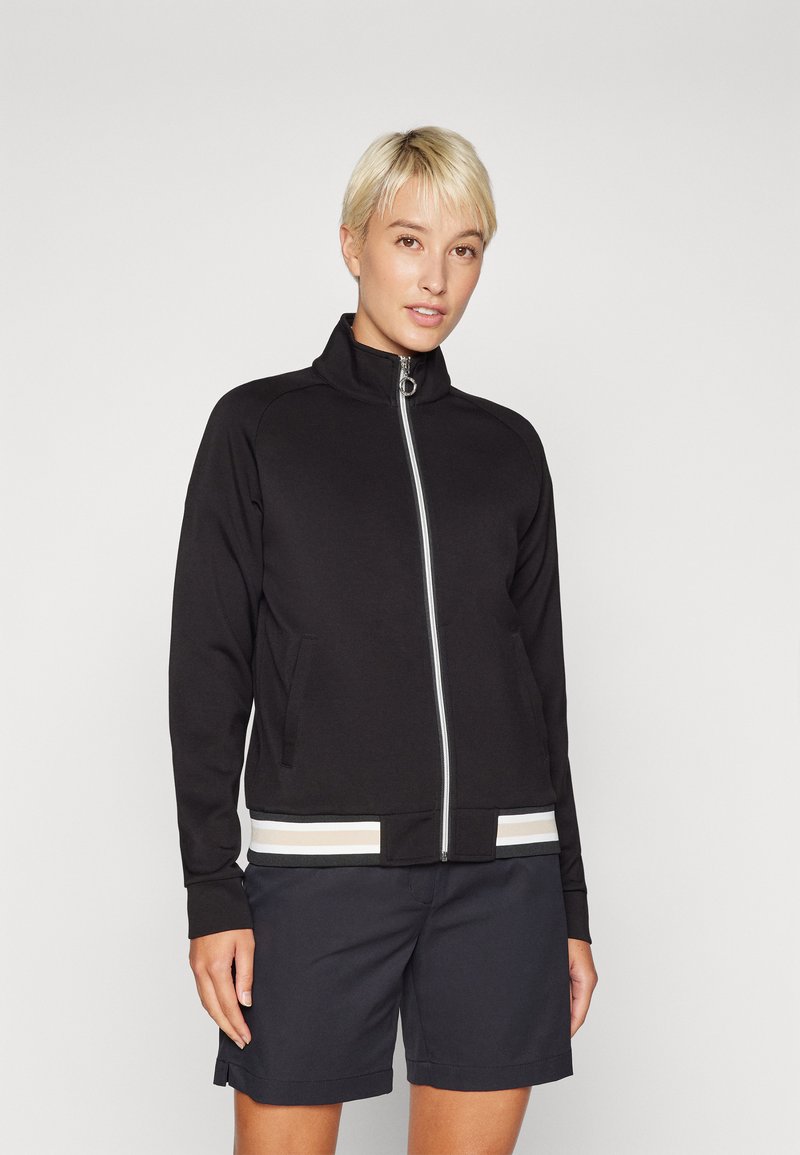 Black zip-up jacket with a stand collar, featuring a contrasting striped waistband. Soft fabric, side pockets, and a simple, fitted design.