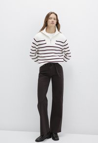 Weiß und burgunderrot gestreifter Strickpullover mit einem halben Reißverschlusskragen, kombiniert mit schwarzen weit geschnittenen Hosen und schwarzen Schuhen. Glatte Texturen, lässiger Schnitt.