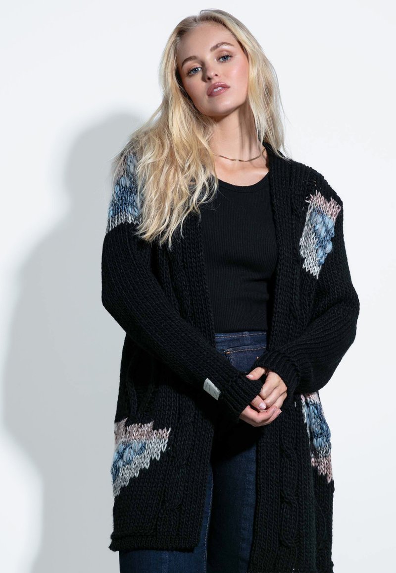 Czarny sweter kardigan z dzianiny, z wzorem w warkocze, z kolorowymi trójkątnymi akcentami na rękawach. Długie rękawy i otwarty przód.
