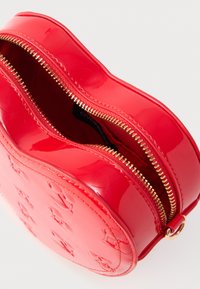 Κόκκινη τσάντα χειρός σε κυκλικό σχήμα από δερματίνη με χρυστό φερμουάρ και ανάγλυφο μοτίβο με το λογότυπο. Το εσωτερικό έχει επένδυση και διαθέτει έναν μονό χώρο.