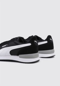 Svarta och vita sneakers med en slät ovandel, mockadetaljer, gummisulor och Puma-logotyp på hälen och sidan. Har en rundad form.