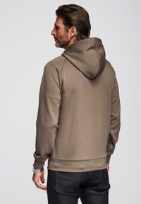 Sudadera con capucha en un color marrón neutro, fabricada con una tela suave de textura lisa, que cuenta con un bolsillo tipo canguro y puños acanalados.