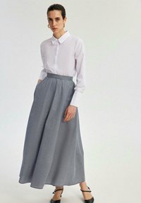 Bela srajca s gumbi, v kombinaciji z dolgo plisirano krilom v modro-beli houndstooth vzoru, ki ima stranske žepe, in črnimi čevlji z zapestnim trakom.