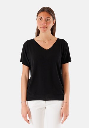 Top nero a maniche corte con scollo a V realizzato in tessuto morbido; presenta una vestibilità rilassata e orlo a costine, abbinato a pantaloni di colore chiaro.