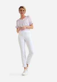 Helllila kurzärmliges Oberteil mit V-Ausschnitt, kombiniert mit taillierten weißen Hosen und weißen Sneakers. Angenehme Textur, lässige Passform.