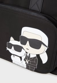 Zwarte stoffen tas met een cartoonontwerp van een man en een witte kat in zonnebrillen, omlijnd in zwart met opvallende accenten. Ritsluiting zichtbaar.
