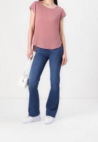 Top rosa a maniche corte con scollo rotondo, abbinato a pantaloni in denim blu a campana e sneakers bianche. Porta una borsa bianca.