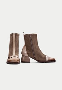 Botines de ante marrón con una punta de charol beige y tacón, que cuentan con cierres de cremallera lateral y detalles texturizados.