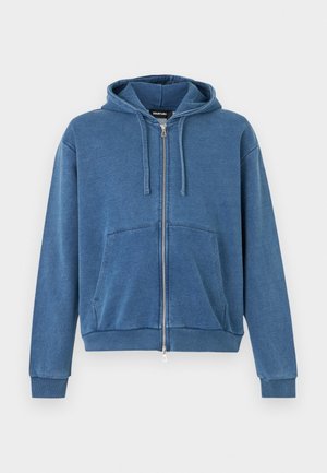 Sweat à capuche zippé bleu avec poches avant, capuche à cordon réglable, poignets et ourlet côtelés, présenté sur un fond uni.