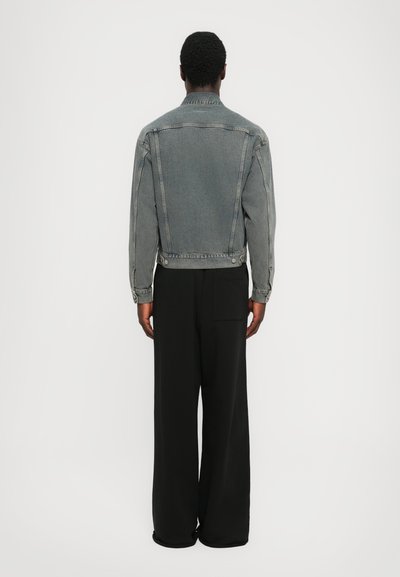 Jachetă din denim gri cu o croială boxy, închidere cu nasturi și buzunare laterale, purtată cu pantaloni negri largi. Fără modele sau accente vizibile.