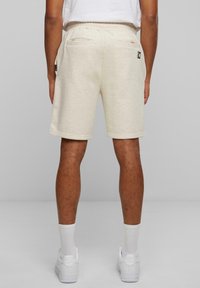 Shorts en coton beige clair avec une taille élastique, des poches latérales, et un logo minimaliste sur l'arrière. Texture lisse.