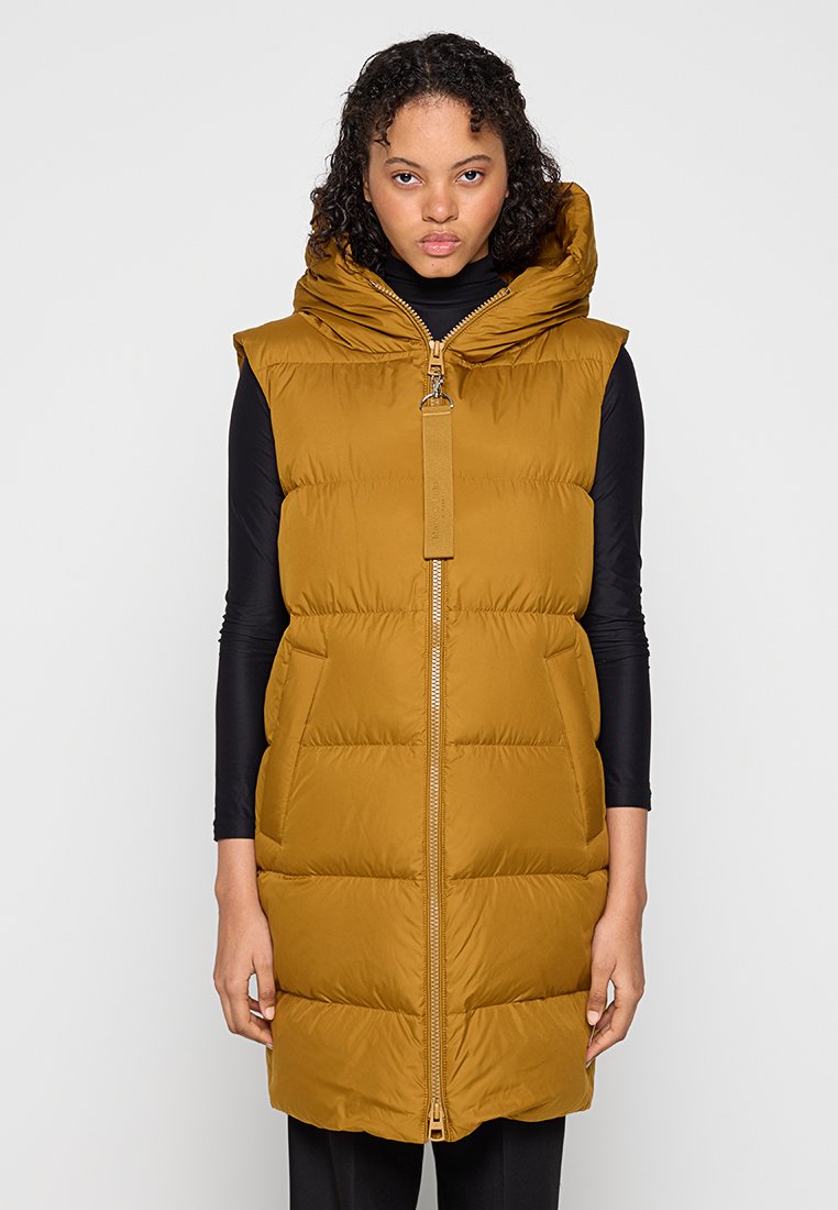 Kurtka puchowa w musztardowym kolorze z zamkiem błyskawicznym z przodu, dużym kapturem i bocznymi kieszeniami. Posiada pikowany wzór i metalowe detale.