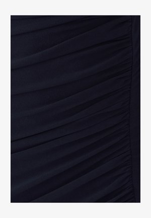 Tumši zila kleita ar mīkstu, teksturētu audumu; tai ir vertikāls ruche pa sāniem, radot piegulšanu siluetu. Nav papildu akcentu.