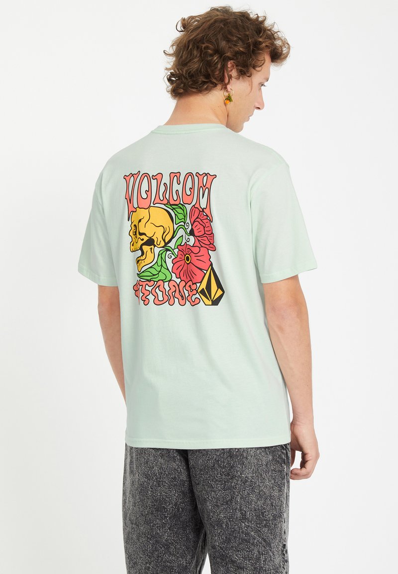 Camiseta verde menta con un gráfico colorido en la parte posterior que incluye una calavera, flores y la palabra "VOLCOM". Corte relajado, mangas cortas, material de algodón.