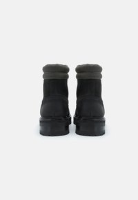 Stivaletti neri in suede con colletto imbottito, parte superiore texturizzata e una spessa suola in gomma nera, caratterizzati da una punta rotonda.