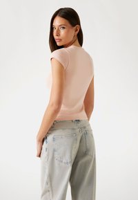 Korte mouwen, lichtroze fitted top gecombineerd met lichtblauwe high-waisted jeans met standaard achterzakken en een ontspannen pasvorm.