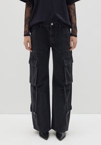 Pantalones cargo negros con un diseño de pierna ancha, que cuentan con múltiples bolsillos frontales, un ligero desvanecimiento y detalles de cremallera en el dobladillo.