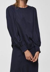 Marinblus med långa puffärmar och rund halsringning. Mjukt, slätt tyg med avslappnad passform, med subtila detaljer vid axlarna.