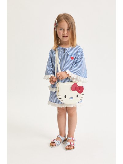 Νεαρή κοπέλα με μπλε και λευκό ριγωτό φόρεμα με δαντέλα, κρατώντας μια λευκή τσάντα Hello Kitty, φορώντας σανδάλια με αγκράφες.