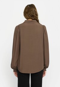 Brun, lätt blus med en avslappnad passform, krage och puffärmar. Ruched-detaljer längs axlar och manschetter.