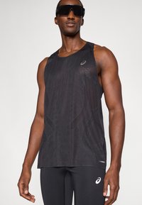 Μαύρη αμάνικη μπλούζα με υφή δικτυωτού σχεδιασμού, με διακριτικό λογότυπο και αντίθετα στοιχεία. Συνδυάζεται με μαύρες κολάν που εφαρμόζουν.