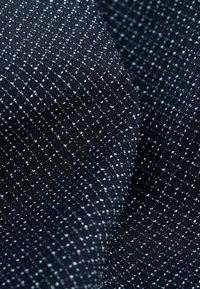 Granatowa tekstura materiału z siatką wzoru i małymi białymi kropkami, tworząca kontrast w szczegółach powierzchni. Miękka i tkana tekstura.