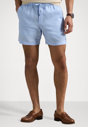 Jasnoniebieskie szorty kąpielowe z elastycznym paskiem w talii, przednim sznurkiem i małym logo. Noszone z brązowymi skórzanymi loafersami.