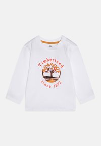 T-shirt blanc à manches longues pour tout-petits avec le logo arbre Timberland en orange et noir et le texte "Timberland depuis 1973" sur le devant, boutons-pression à l'épaule.