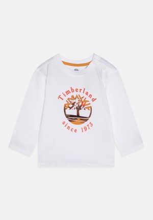 Camiseta de manga larga blanca para niño pequeño con el logo del árbol de Timberland en naranja y negro y el texto "Timberland desde 1973" en el frente, con botones a presión en el hombro.
