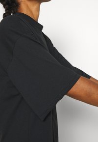 Camiseta negra de gran tamaño con un cuello alto y mangas cortas anchas, hecha de suave tela de algodón, con líneas limpias y costuras mínimas.