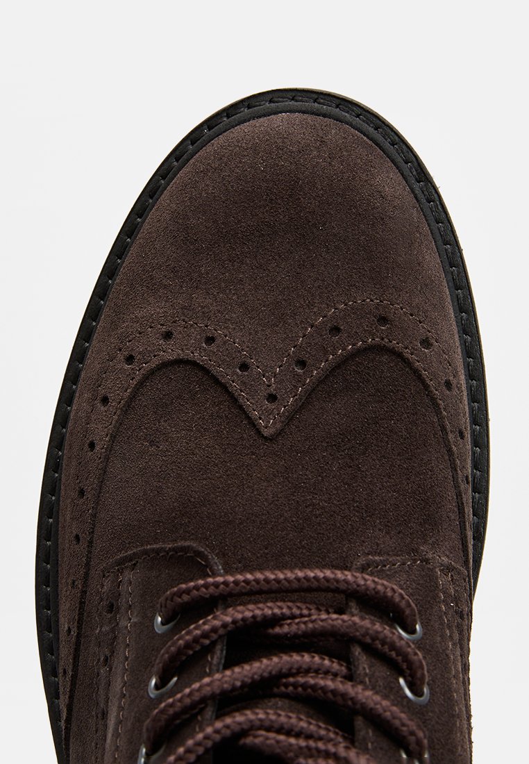 Braunes Wildlederschuh mit Brogue-Design. Verfügt über dekorative Perforationen, runde Schnürsenkel und eine kontrastierende schwarze Gummisohle.