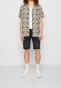 Camicetta nera a maniche corte con motivo floreale bianco e giallo, abbinata a pantaloni corti di jeans arrotolati e sneakers bianche. Canottiera bianca semplice sotto.