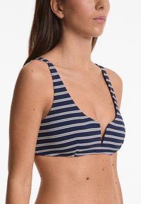 Top bikini a righe navy e bianche con scollatura a V profonda, spalline larghe e tessuto testurizzato. Presenta un motivo a righe a contrasto.