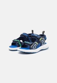 Sandale bleu marine avec des sangles en velcro et des accents verts, dotée d'une semelle intérieure bleue rembourrée et d'une semelle extérieure en caoutchouc blanche. Design léger.