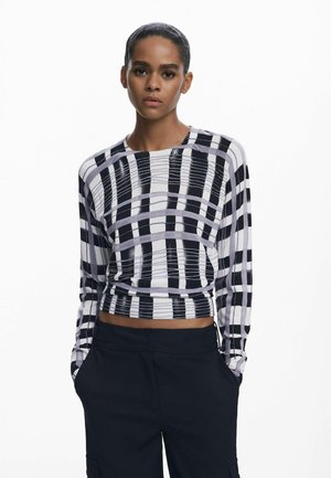 Long-sleeve cropped top in black and white plaid pattern, featuring textured fabric and a round neckline. Paired with dark trousers.