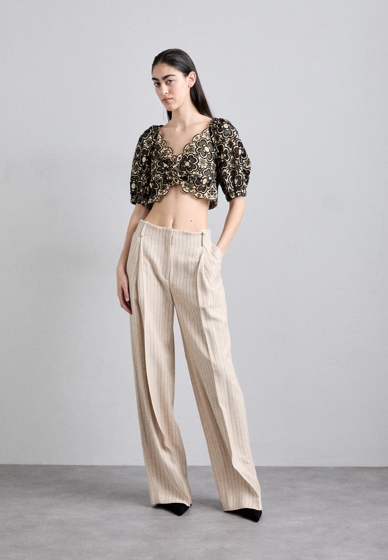 Black and gold floral crop top with puff sleeves, paired with beige pinstriped high-waisted trousers and black pointed heels.