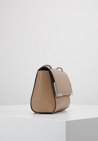 Borsa a mano strutturata beige con una superficie liscia, accessori in argento e una tracolla a catena, caratterizzata da una forma angolare distintiva e dettagli neri.