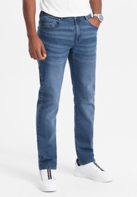 Vaqueros de mezclilla azul oscuro con corte recto, que cuentan con un diseño clásico de cinco bolsillos y líneas de textura sutiles. Combinados con zapatillas blancas.