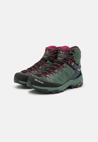 Green hiking boots with dark accents, mesh panels, and a high ankle design. Features textured surface and patterned rubber sole for grip.