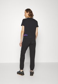 Camiseta negra de manga corta con un gráfico de ola púrpura en la espalda, combinada con pantalones de chándal negros ajustados y zapatillas deportivas negras.