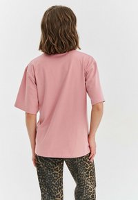 Světle růžové oversized tričko s krátkým rukávem, hladkou texturou a kulatým výstřihem, doplněné o kalhoty s leopardím printem.