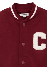 Giacca varsity bordeaux con colletto a righe bianche, chiusura con bottoni e una "C" bianca ricamata sul lato sinistro. Texture del tessuto morbida.
