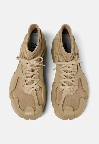 Zapatillas beige con un tejido de punto texturizado y una superposición de goma moldeada, que cuentan con cordones gruesos y una puntera redondeada. Diseño único con elementos recortados.