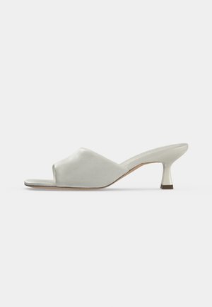 Zapato mule blanco de punta abierta con un tacón bajo y curvado tipo kitten y material superior liso, mostrado en perfil lateral sobre un fondo liso.